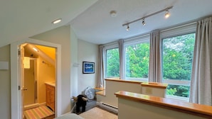A bedroom with a large window, a bed, a bedside table, a fan, and a door leading to a bathroom. - R21 Completely Renovated Bretton Woods Condo, AC, Unbeatable Ski-in Ski-out Location! Fast Wifi (Bretton Woods)