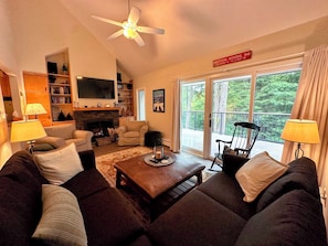 A cozy living room with a fireplace, comfortable seating, and a balcony with a view of the forest. - R21 Completely Renovated Bretton Woods Condo, AC, Unbeatable Ski-in Ski-out Location! Fast Wifi (Bretton Woods)