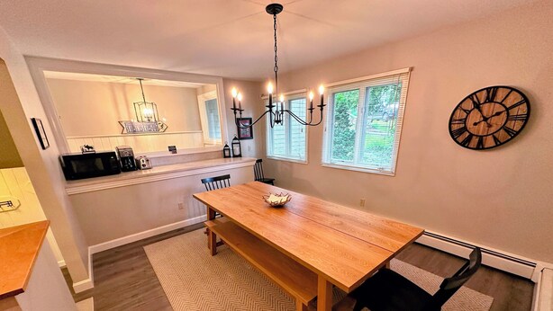 A dining area with a wooden table, black chairs, a chandelier, and a clock on the wall. - R21 Completely Renovated Bretton Woods Condo, AC, Unbeatable Ski-in Ski-out Location! Fast Wifi (Bretton Woods)