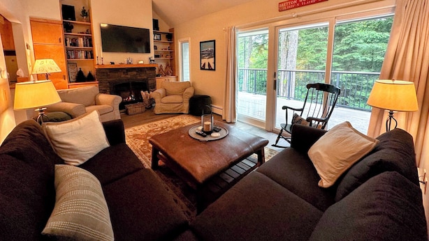 A cozy living room with a fireplace, comfortable seating, and a balcony with a scenic view. - R21 Completely Renovated Bretton Woods Condo, AC, Unbeatable Ski-in Ski-out Location! Fast Wifi (Bretton Woods)