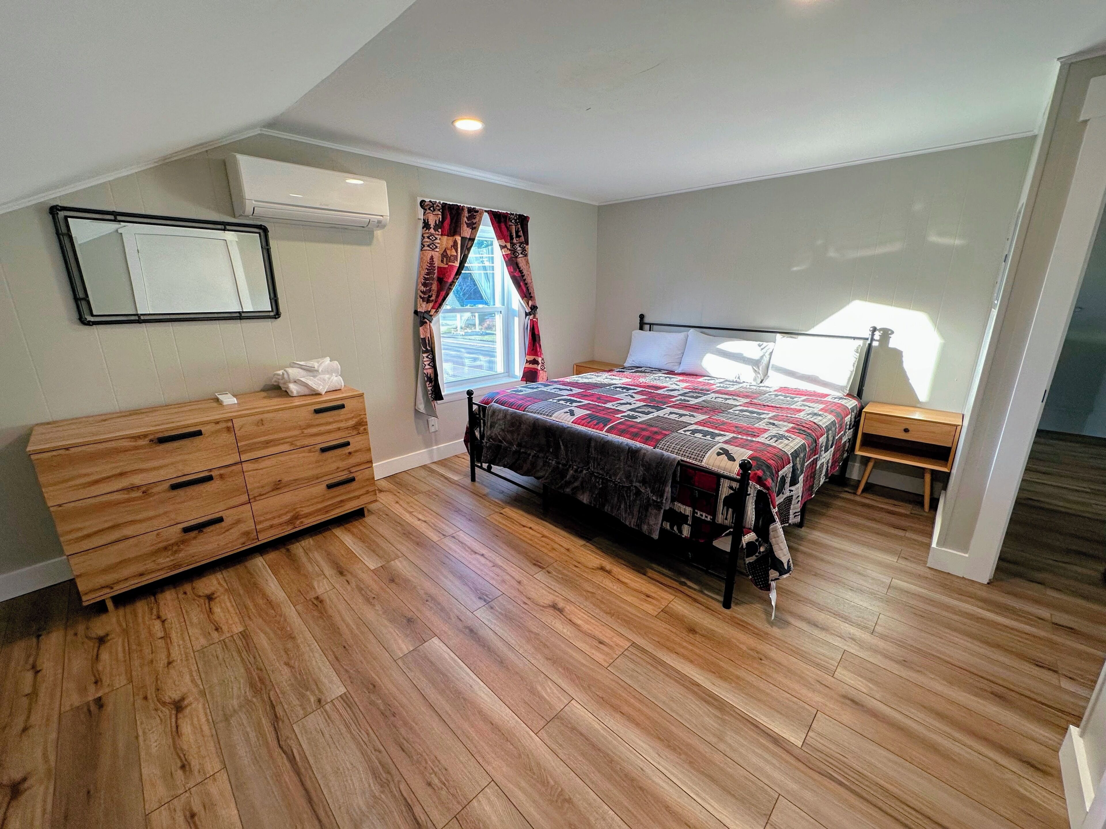 Ein Schlafzimmer mit einem Holzkleiderschrank, einem Bett mit einem gemusterten Bettbezug, einem Fenster mit Vorhängen und einem Deckenventilator.