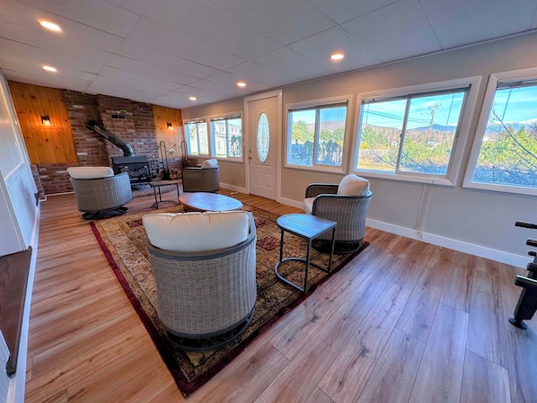 A cozy living room with wicker furniture, a fireplace, and large windows offering a view of the outdoors.