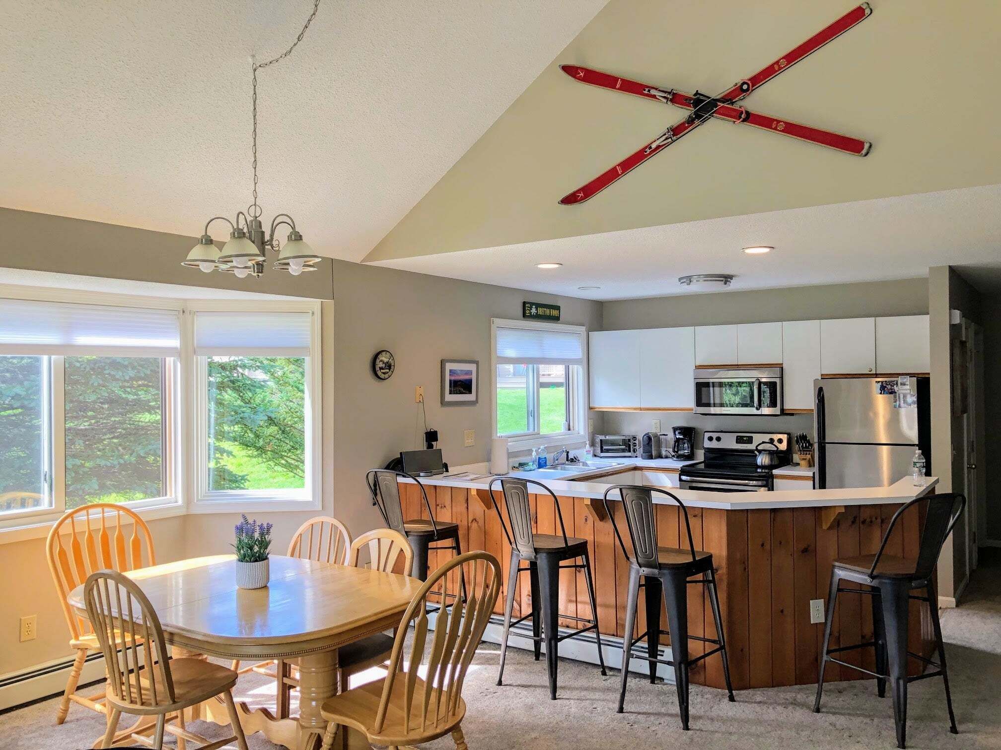 A kitchen with a central island, wooden chairs, a dining table, and a ceiling-mounted ski rack.