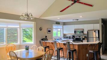 A kitchen with a central island, wooden chairs, a dining table, and a ceiling-mounted ski rack.