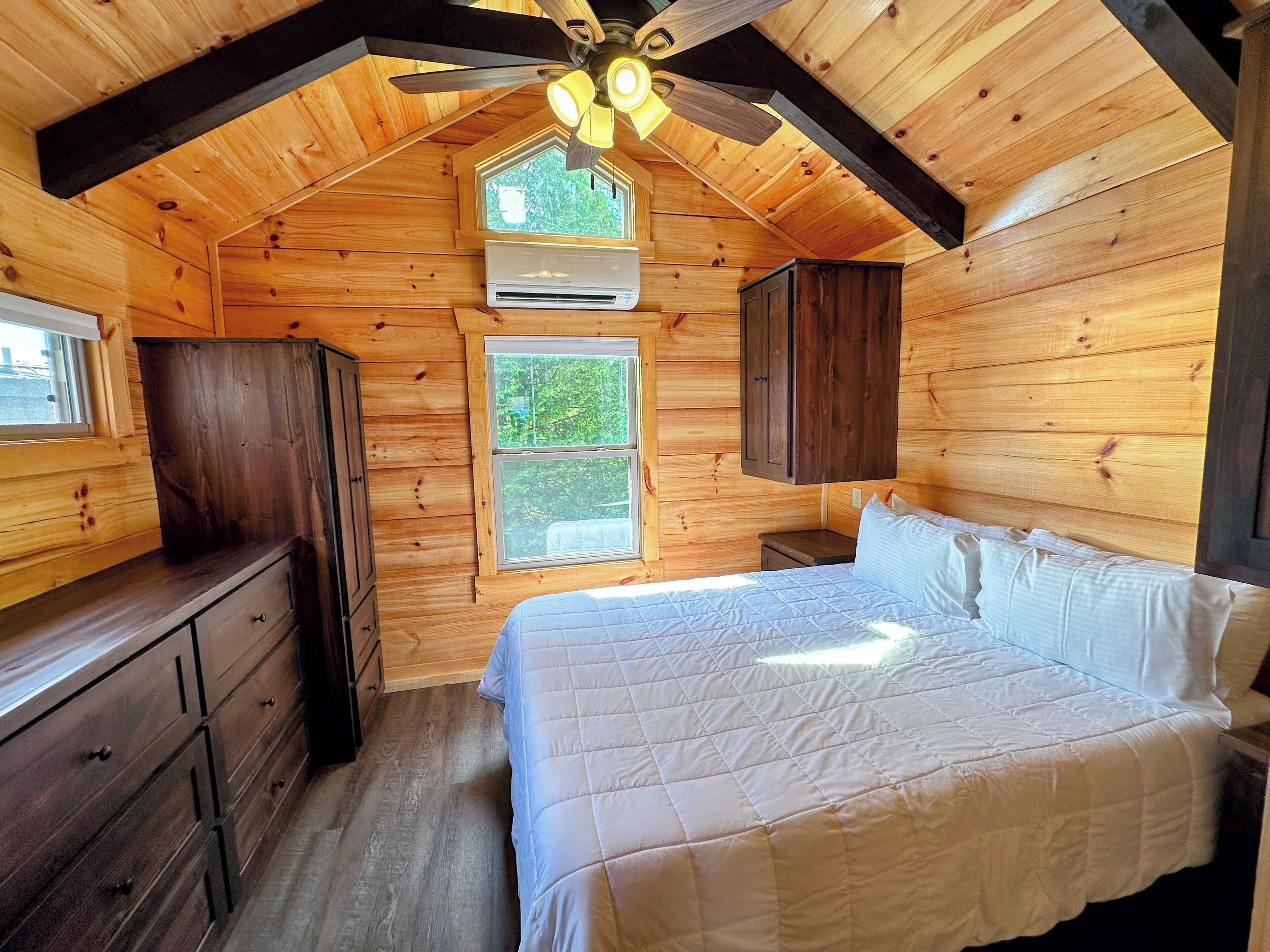 A wooden cabin bedroom with a bed, dresser, and built-in cabinets.