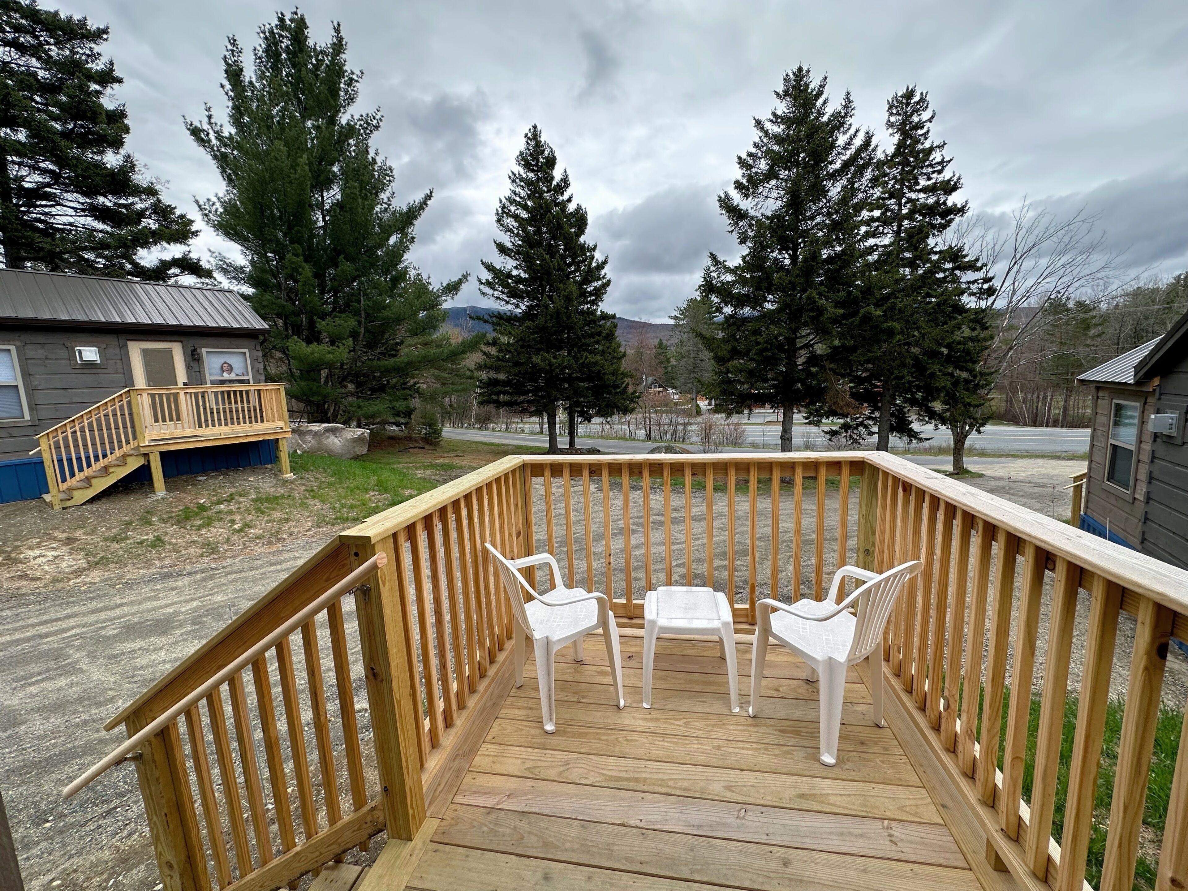 A wooden deck with a table and chairs, overlooking a road and trees.