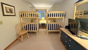 A narrow hallway with bunk beds on either side, a wooden chair, a desk with a computer, and a TV. - Sc10 Cozy Bretton Woods Ground Level Condo (Bretton Woods)