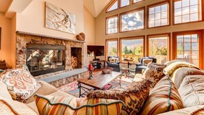 A cozy living room with a stone fireplace, comfortable seating, and large windows offering a view of the outdoors. - SH4 Bretton Woods Condo With Hot Tub, Next to Skiing and Mt Washington Hotel, ski Slopes Views! (Bretton Woods)