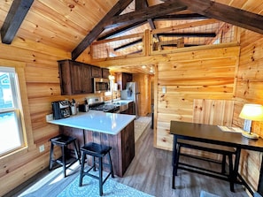 A wooden cabin with a kitchen featuring a central island, bar stools, and a dining table.