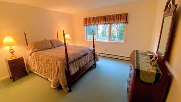 A bedroom with a four-poster bed, a dresser, a mirror, and a window with curtains.
