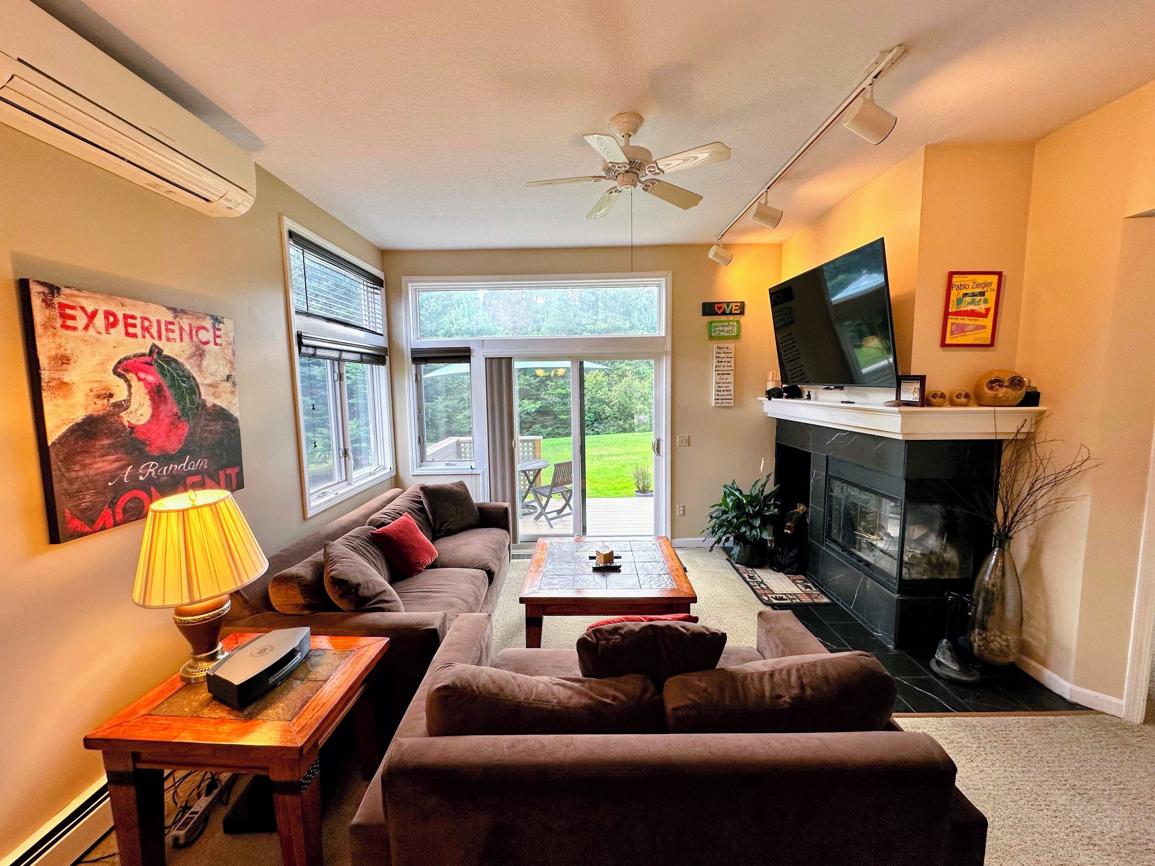 Una sala de estar con sofá, mesa de centro y chimenea. Hay un televisor en la pared y una ventana con persianas.