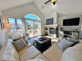 Un salón amplio con chimenea, televisor y un ventanal que ofrece vistas al exterior.