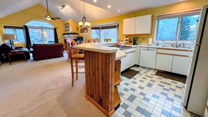 Eine Küche mit Kochinsel, Holzschränken, einem Essbereich mit einer Couch und großen Fenstern.