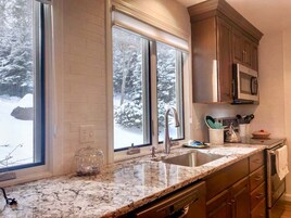 Una cocina con encimera de granito, electrodomésticos de acero inoxidable y una ventana con vistas nevadas.