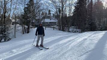 A person skiing on a snow-covered path with trees and a building in the background.