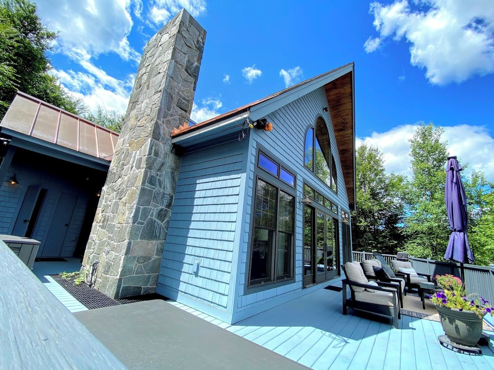 A modern house with a stone pillar, large windows, and a deck with outdoor furniture.