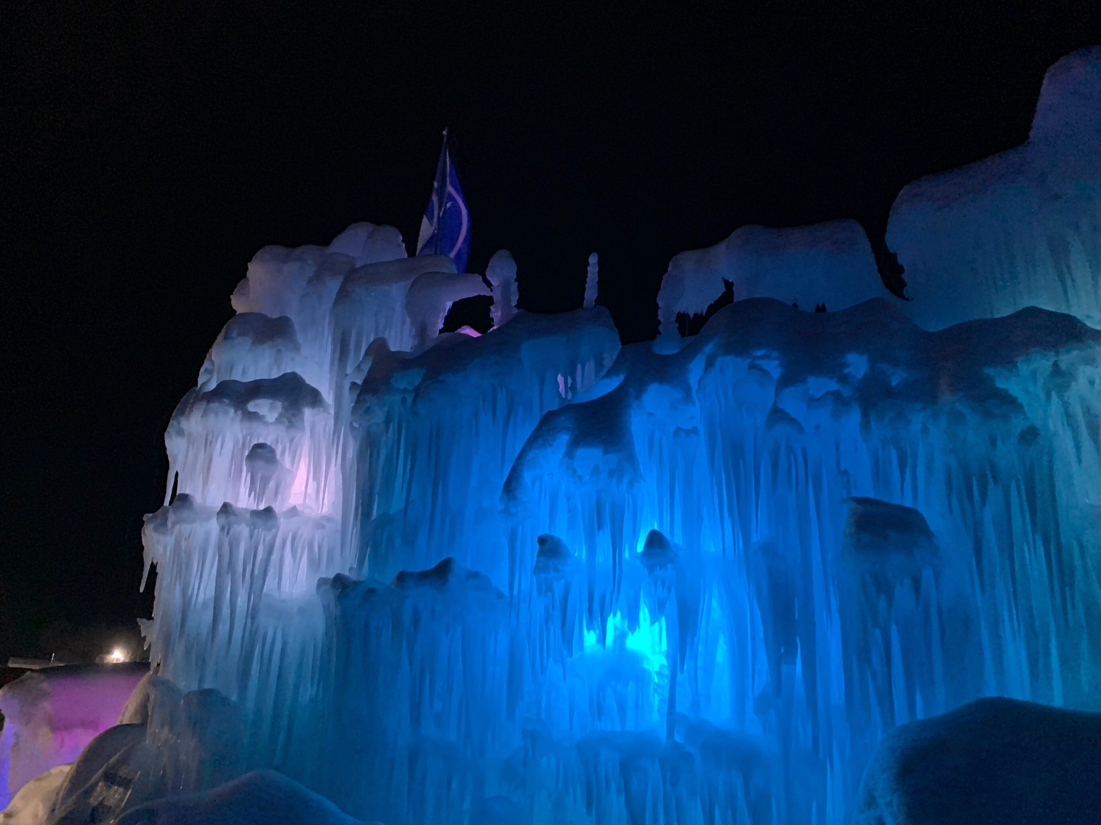 Une sculpture de glace surmontée d’un drapeau, illuminée par des lumières bleues et violettes.