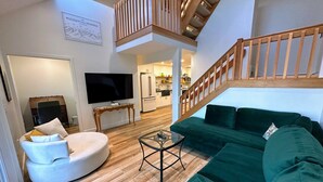 A living room with a sofa, a TV, a small table, and a staircase. - Rb18 Updated Ski-in Ski-out Bretton Woods Townhome (Bretton Woods)