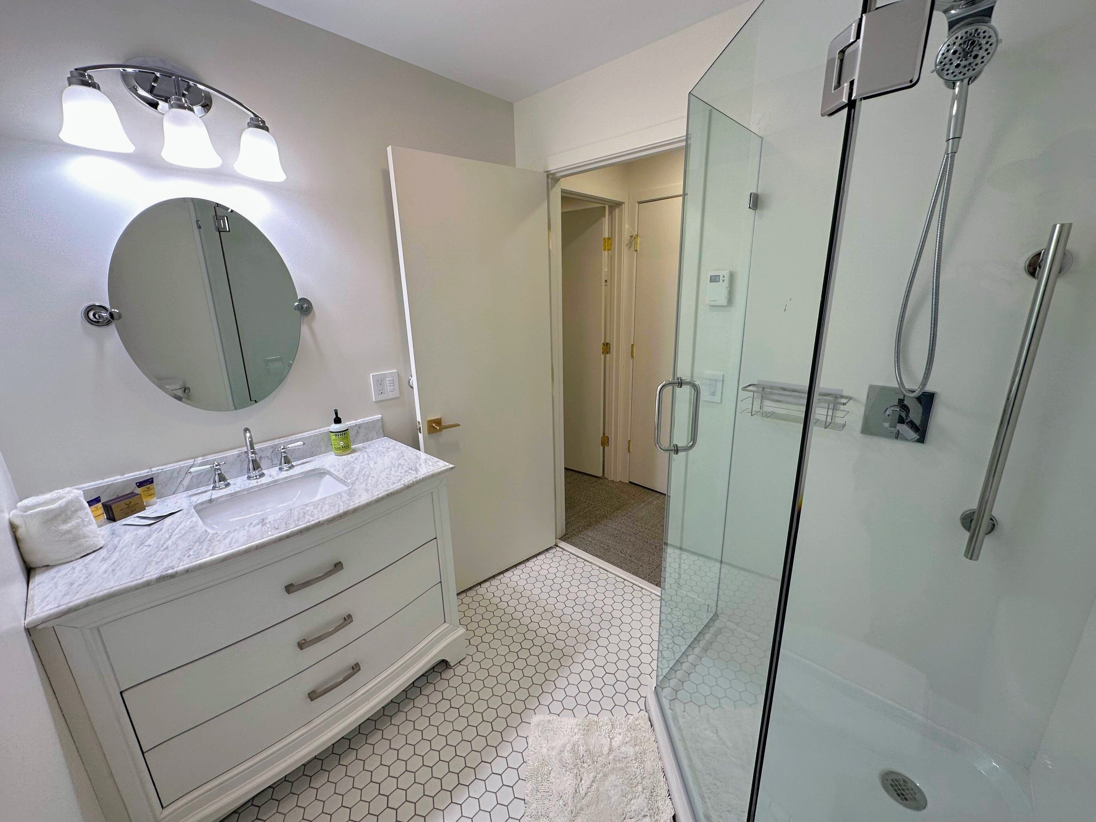 A modern bathroom with a glass shower enclosure, a vanity with a mirror and two sinks, and a hexagonal tile floor.