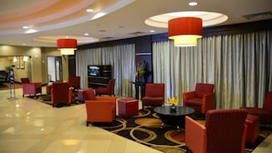 Un hall d’hôtel avec des fauteuils à revêtement rouge, une table basse noire et un grand luminaire suspendu rouge.