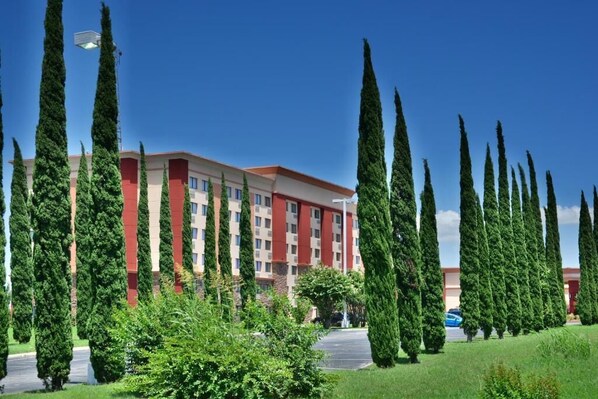Un hôtel à plusieurs étages, doté d’une façade rouge et beige, entouré de grands arbres élancés.
