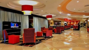 Un hall d'hôtel avec des sièges rouges, un écran de télévision et un design moderne au niveau du plafond.