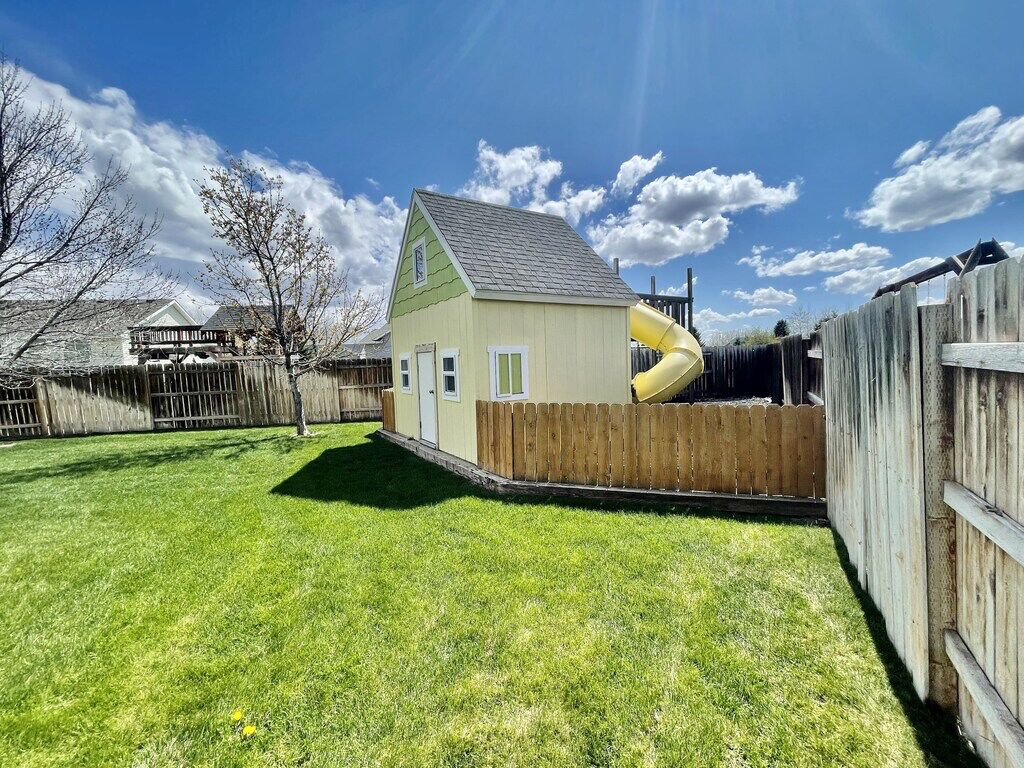 A house with a yellow slide attached to a wooden fence.
