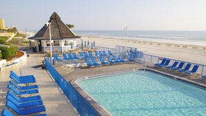 A pool area with blue lounge chairs and a small building with a thatched roof. - Best Place to Stay for the Jeep Beach Week at Daytona Beach, FL - 1 BD/1 BA (Daytona Beach)
