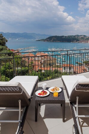 Ein Balkon mit Frühstückstisch mit Blick auf einen Hafen voller Boote und eine Küstenstadt.