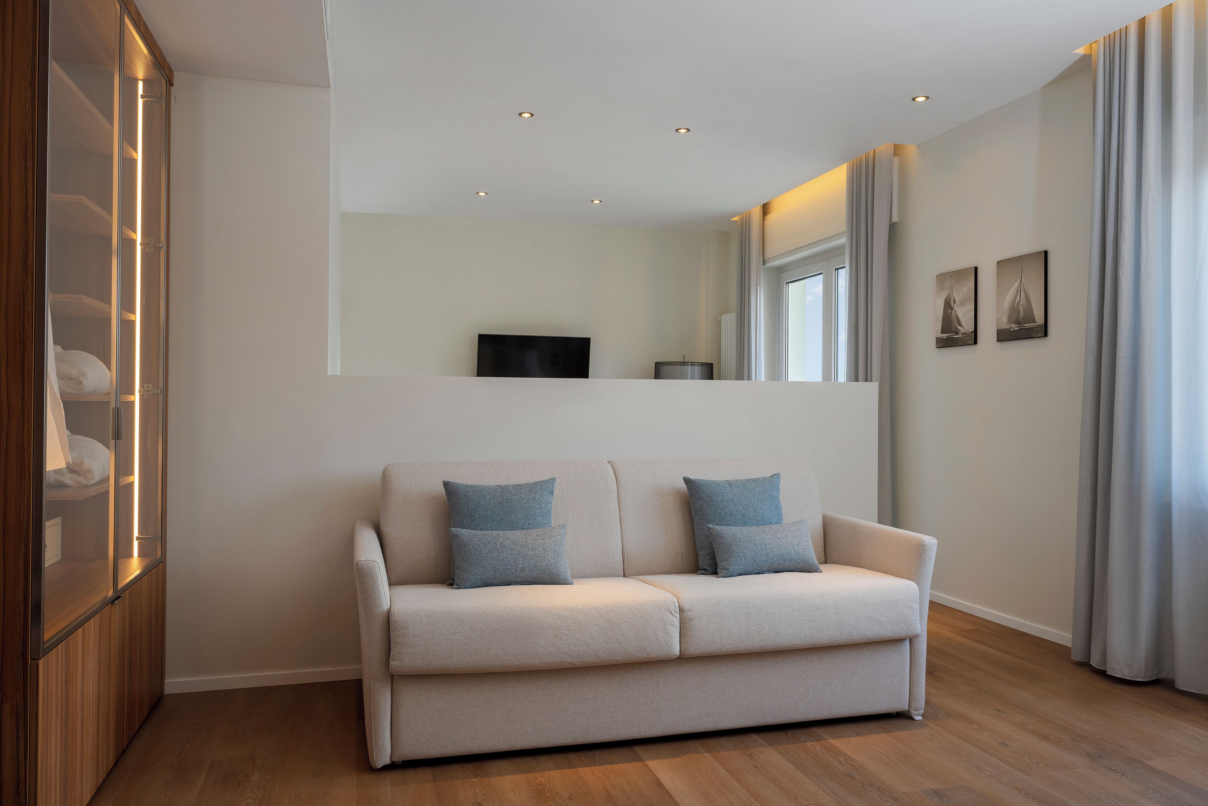 A modern living room with a beige sofa, two cushions, a TV, and a large window with curtains.