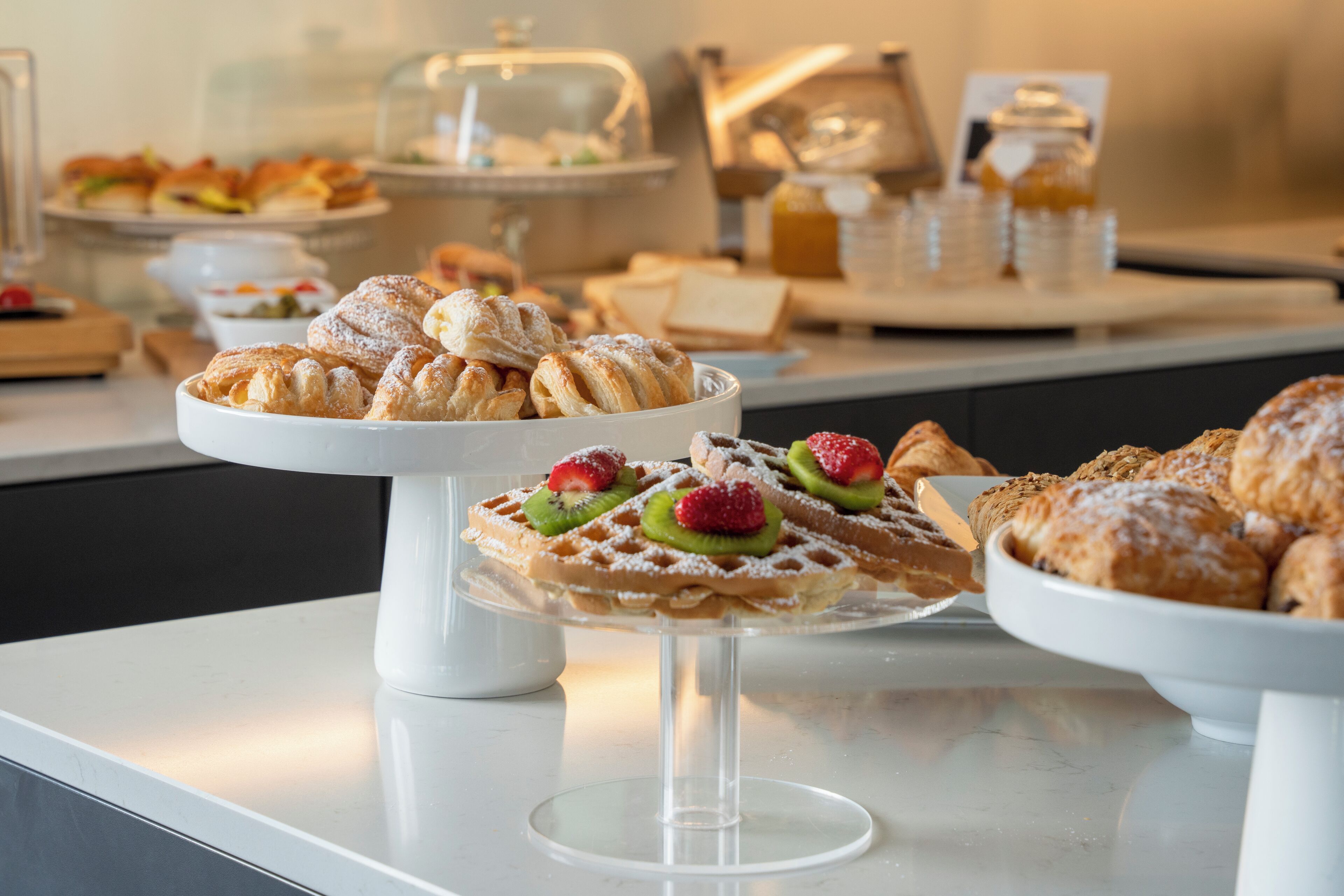 Ein reichhaltiges Buffet mit verschiedenen Backwaren und Desserts, darunter Waffeln und Gebäck mit Früchten und Puderzucker.