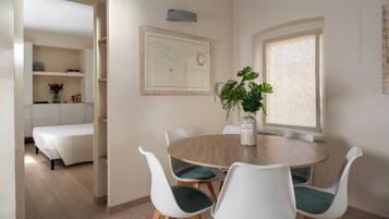 A dining area with a round table, white chairs, a potted plant, and a map on the wall.