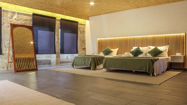 A modern bedroom with two beds, a stone wall, and a wooden ceiling. - FONTE DA ROSA GUEST HOUSE CENTRAL STUDIO (Belmonte)