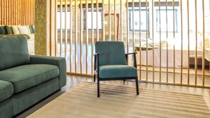A modern living room with a green sofa, a teal armchair, and a wooden partition. - FONTE DA ROSA GUEST HOUSE CENTRAL STUDIO (Belmonte)
