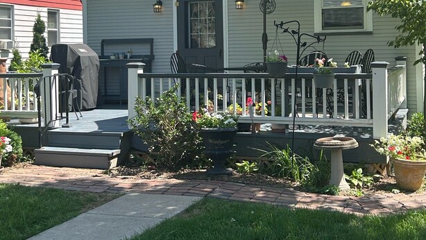Ein Haus mit überdachter Veranda, einem grünen Sonnenschirm und einem Garten mit Topfpflanzen.