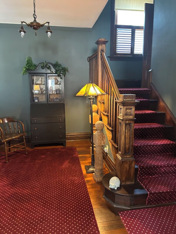 A staircase with wooden railings and red carpeted steps, a wooden bench, a cabinet with glass doors, and a chandelier.