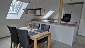Una cocina moderna con una isla central, una zona de comedor con una mesa y sillas de madera, y un tragaluz sobre la mesa.