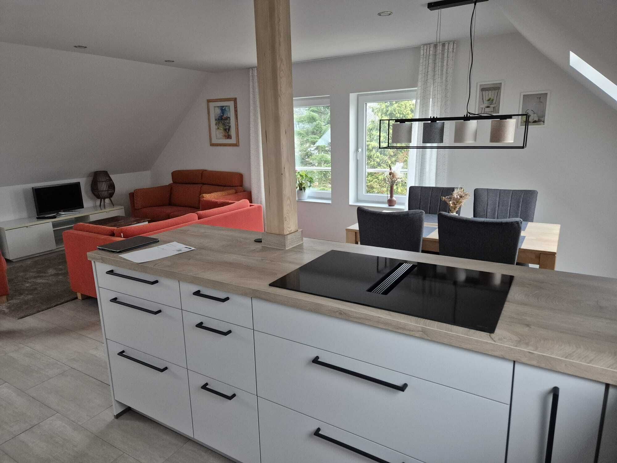 A modern kitchen with a central island, a dining area with a table and chairs, a sofa, and a TV.
