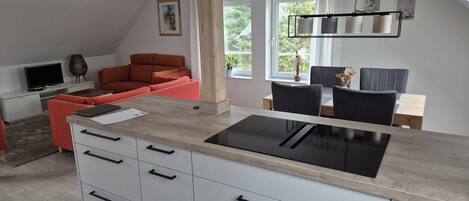 A modern kitchen with a central island, a dining area with a table and chairs, a sofa, and a TV.