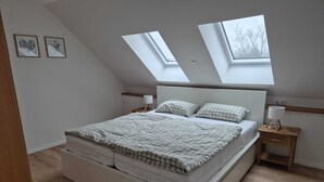 Un dormitorio con cama elevada, tragaluces, una mesita de noche y una mesilla.