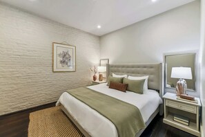 Une chambre d’hôtel avec un mur en briques, un lit recouvert d’une couverture verte, une table de chevet avec une lampe et un miroir.