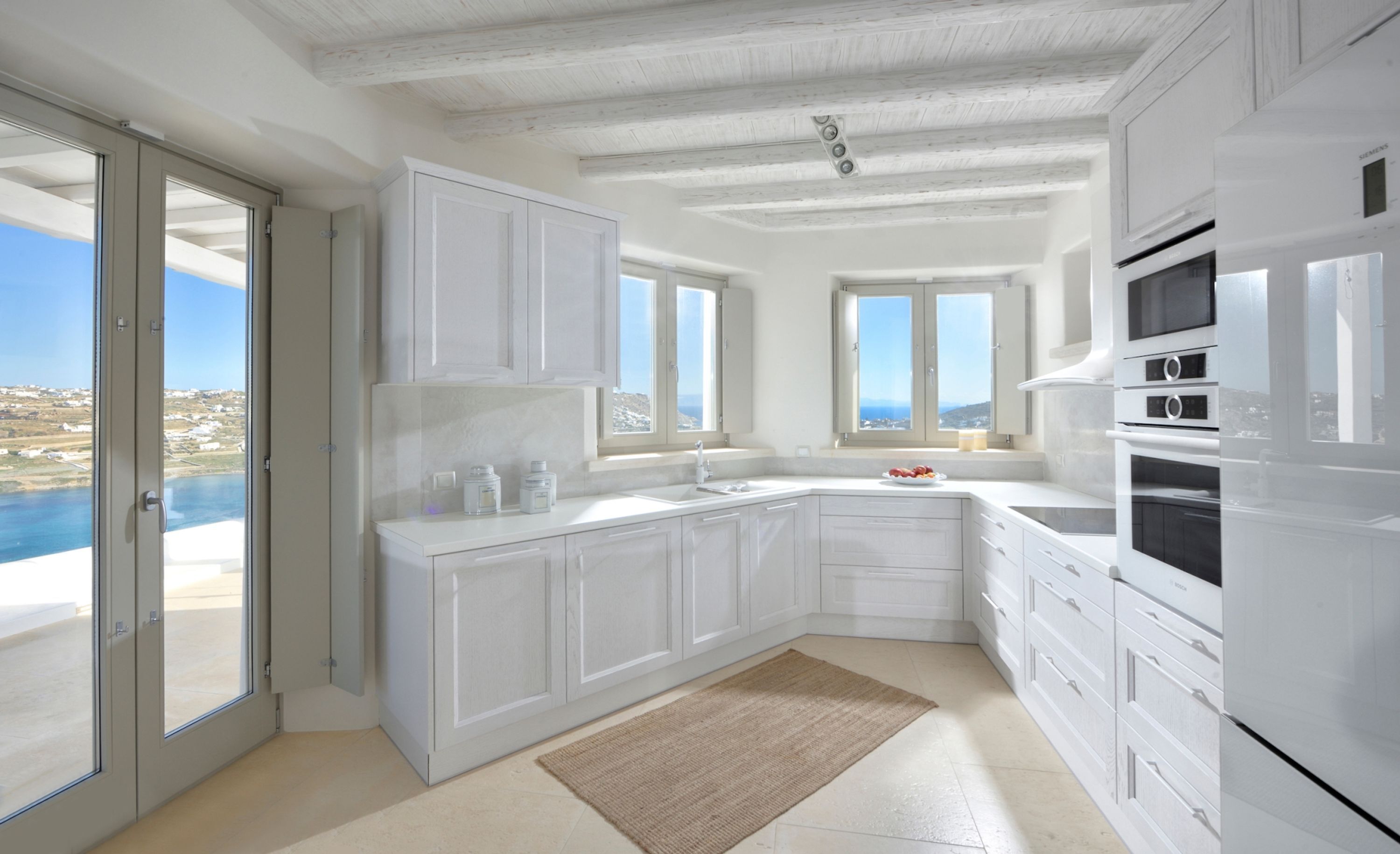 A modern kitchen with white cabinets, a large island, and a view of the sea.