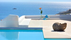 En pool med fri utsikt över havet, en vas med en blomma och en stenskulptur.