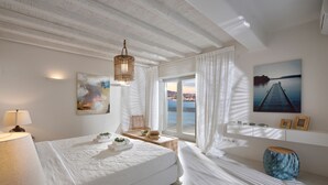 Ett hotellrum med en stor säng, ett skrivbord, en stol, ett fönster med gardiner, ett väggmonterat handfat och en tavla som föreställer en brygga.