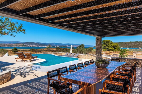 A covered outdoor area with a pool, lounge chairs, and a table with chairs.