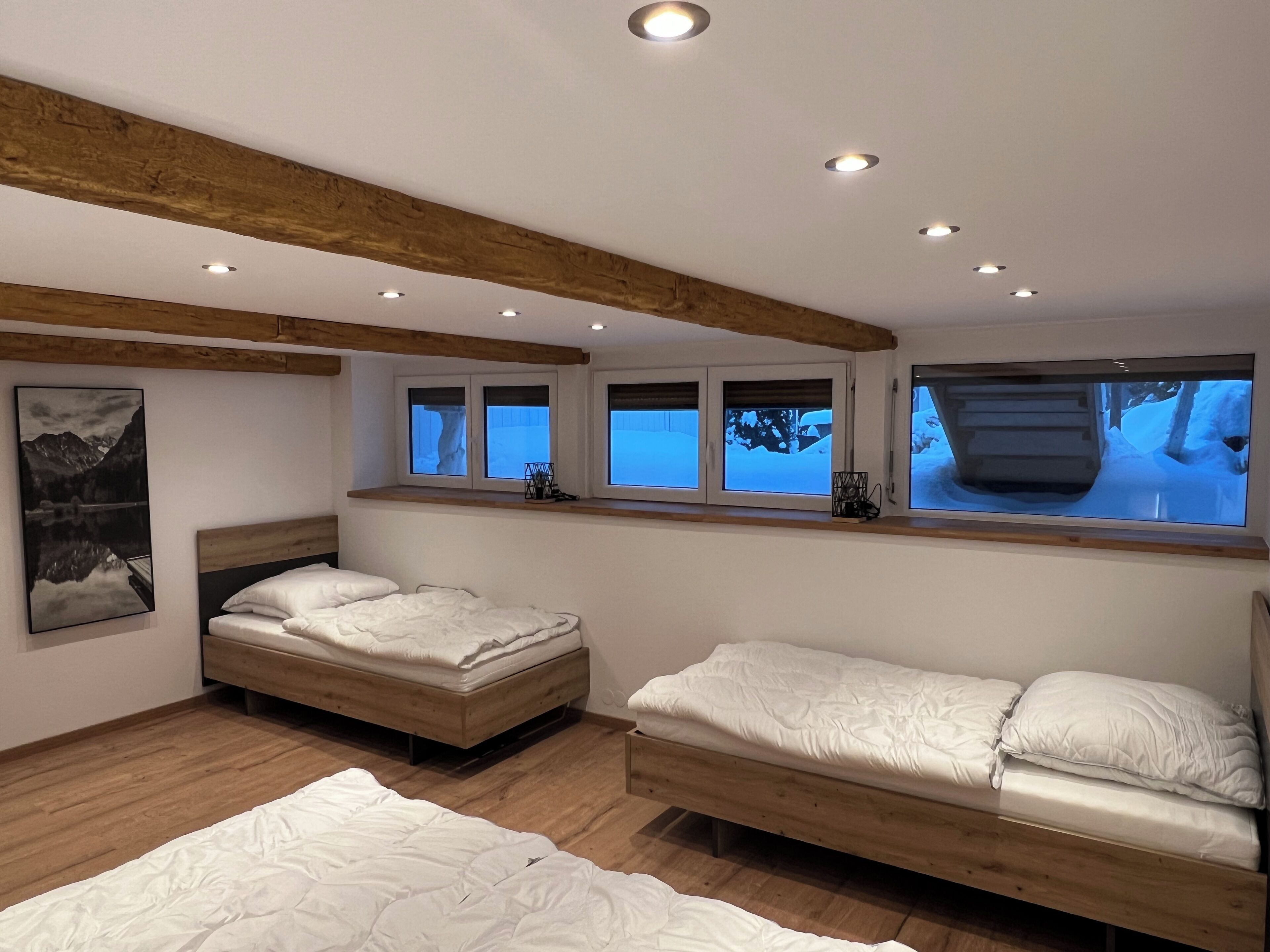 Ein Schlafzimmer mit zwei Betten, Holzbalken, großen Fenstern und einem Gemälde.