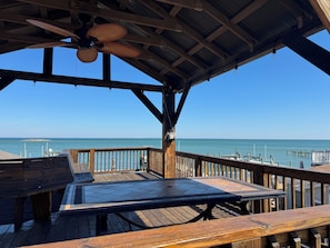 A wooden deck with a table and benches, overlooking a marina with boats.