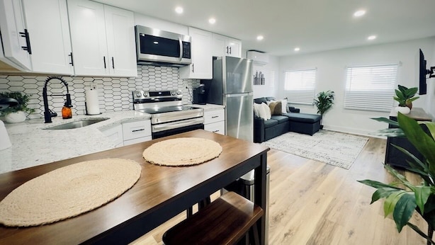 A modern kitchen with white cabinets, stainless steel appliances, and a wooden dining table. - Cozy 1BR in Philly with Rain Shower (Philadelphia)