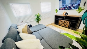 A modern living room with a sectional sofa, a flat-screen TV, and a wooden entertainment unit. - Cozy 1BR in Philly with Rain Shower (Philadelphia)