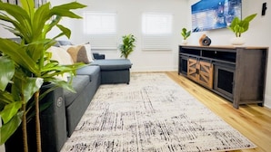 A modern living room with a grey sofa, a patterned rug, and a large cityscape painting on the wall. - Cozy 1BR in Philly with Rain Shower (Philadelphia)
